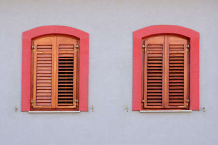 Two red windows with wooden jalousie on white wallの写真素材