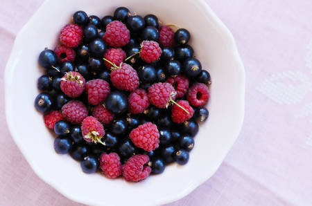 Mix of wild raspberry and black currant in bowl with copy space on pink backgroundの写真素材