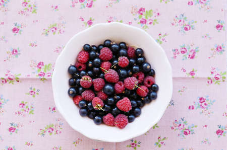 Mix of wild raspberry and black currant in bowl with copy space on flower background
