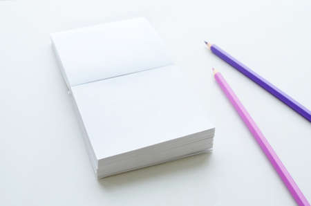 Empty note paper block and two pencils on light background