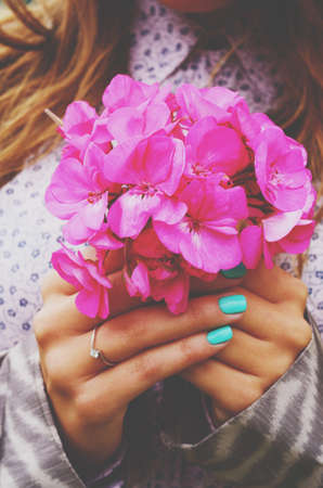 Stylish lady holding bunch of pink flowers in her hands with teal manicureの写真素材