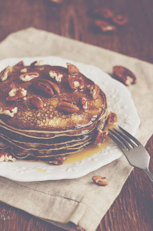 Stack of homemade thin pancakes topped with honey and pecan nuts on brown wooden tableの写真素材