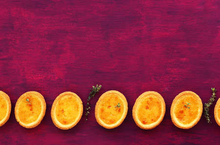 Mini lemon tartlets with thyme with empty space on fuchsia color background