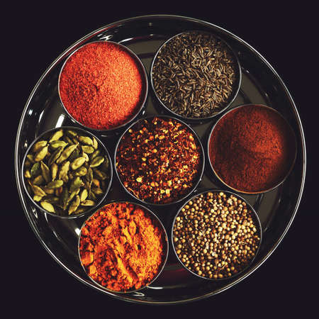 Set of indian spices in metal bowls - green cardamom, turmeric powder,  coriander seeds, cinnamon, cumin, and chili on black backgroundの写真素材