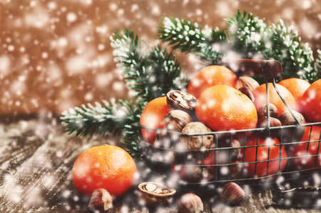 Christmas decoration with ripe tangerines in wire basket, walnut, hazelnut,  pine tree twigs and snowflakes with copy space on wooden backgroundの写真素材