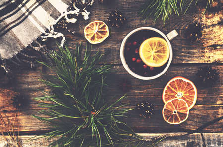 Winter drink with lemon, cranberries and spices, pine tree twigs and checked plaid on wooden...