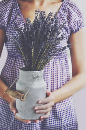 Woman holding bunch of lavender flowers in vintage milk churnの写真素材