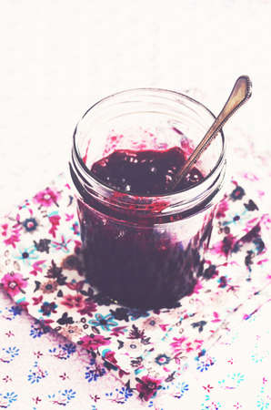 Homemade wild blueberry jam in glass jar at floral table cloth