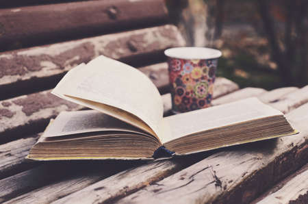 Open book and hot drink on wooden bench in autumn gardenの写真素材
