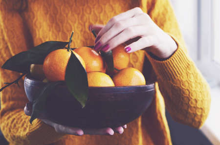 Girl at home holding wooden bowl full of fresh winter tangerinesの写真素材