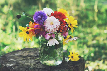 Bunch of flowers in glass jar on tree stub, summer backgroundの写真素材