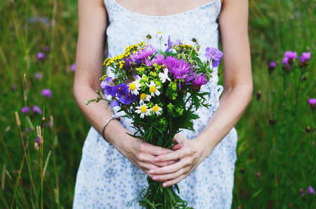 Woman in country style dress holding bunch of colorful flowers in summer fieldの写真素材