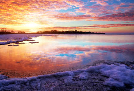 Winter landscape with lake and sunset fiery sky. Composition of nature. の写真素材