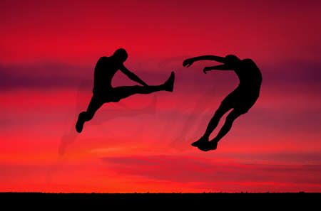 Silhouettes of two fighters on sunset fiery background. Battle at sunset. Kick in the air at the opponent's body.の写真素材