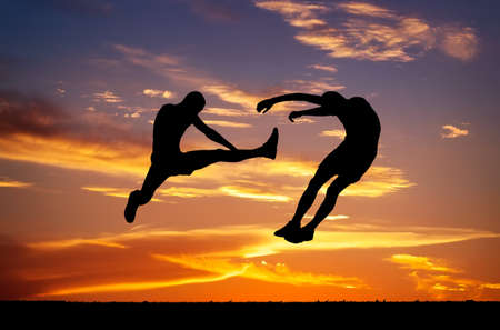 Silhouettes of two fighters on sunset fiery . Battle at sunset. Kick in the air at the opponent\'s body.の写真素材