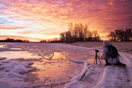 Photographer take pictures on the river bank in winter. Girl, photographed sunsetの写真素材