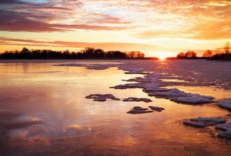 Winter landscape with lake and sunset fiery sky. Composition of nature.の写真素材