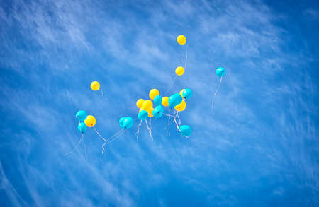 Yellow and blue balloons flying up in the skyの写真素材
