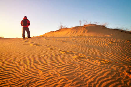 Sandy desert and man in winter clothes standing at a dune top