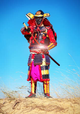 Man in samurai costume pulls out his powerfull hot sword. Men in samurai on the sand. Original Characterの写真素材