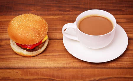 Cup of coffee and Hamburger with fresh tomato, salad, cheese and cutlet on wooden background.の写真素材