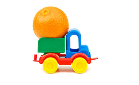 Small plastic colorful toy truck with one big mandarin fruit in basket on white backgroundの写真素材