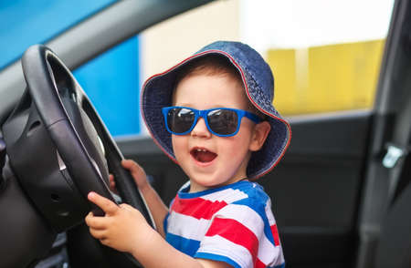 Happy cute little boy with glasses sitting in the car and keeps the wheel