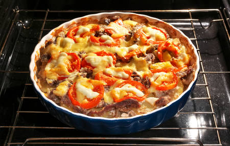 Potato with meat, tomato and cheese is baked in the oven. Cooking with nonstick mold in the ovenの写真素材