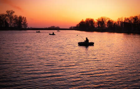 Beautiful landscape with orange sunrise, lake and fishermen in boatsの写真素材