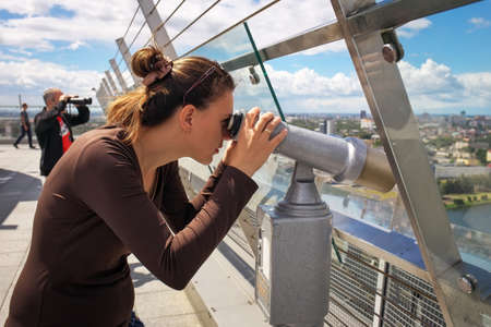 Girl looking through a telescope on the roof of a high building.の写真素材