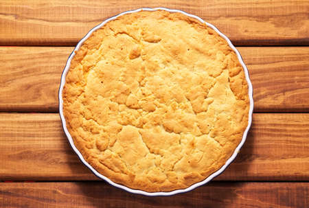 Homemade baked pie in the baking dish on a wooden table. Top view