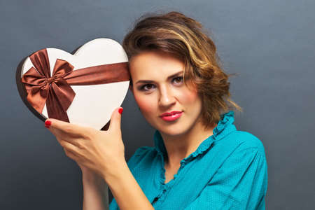 Beautiful girl holding gift in the form of heart on gray backgroundの写真素材