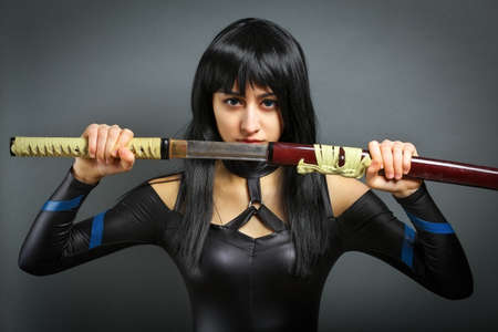 Beautiful girl with sword on grey background. She pulls out the swordの写真素材