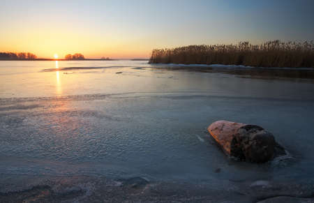 Beautiful winter landscape with stump in the ice and sunset sky.の写真素材