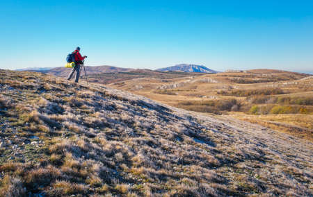 Photographer takes pictures on top of the mountain in autumn. Traveler with backpack enjoying a view from the mountain top

の写真素材