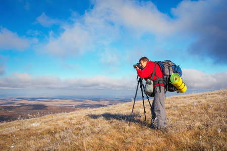 Photographer takes pictures on top of the mountain in autumn. Traveler with backpack enjoying a view from the mountain topの写真素材