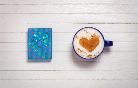 Cup of coffee with heart shape symbol and gift box on wooden white backgroundの写真素材