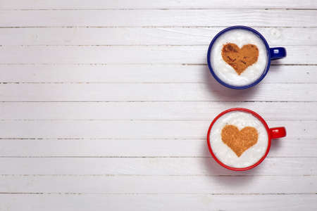 Two cups of coffee with heart shape symbol on wooden white backgroundの写真素材