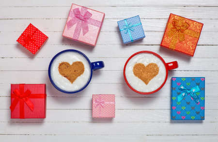 Two cups of coffee with heart shape symbol and gift boxes on wooden white backgroundの写真素材