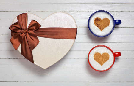 Two cups of coffee with heart shape symbol and gift box on wooden white backgroundの写真素材