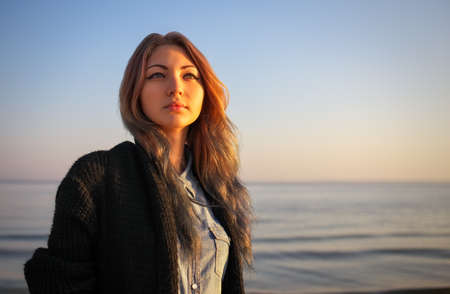 Outdoors portrait of young beautiful girl in autumn near the sea during sunriseの写真素材