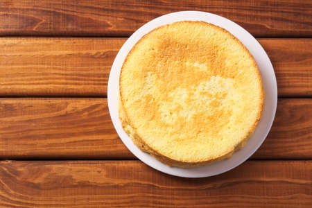 Round homemade biscuit cake made from flour, sugar powder, eggs on a plate on wooden table. The...