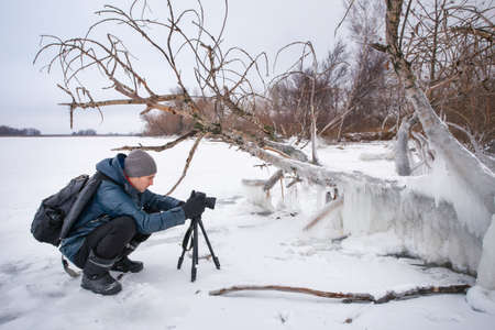 Professional on the lake. Nature photographer takes photos with mirror camera on the river in winter season. の写真素材