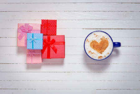 Cups of coffee with heart shape symbol and gift boxes on wooden white backgroundの写真素材