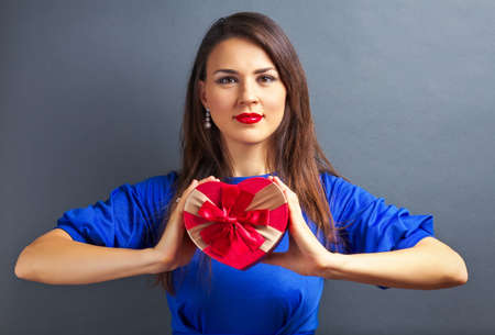 Beautiful girl holding gift in heart form on gray backgroundの写真素材