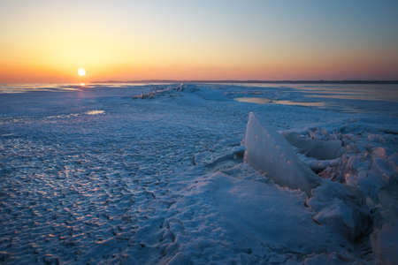 Winter landscape with frozen lake and sunset sky.の写真素材