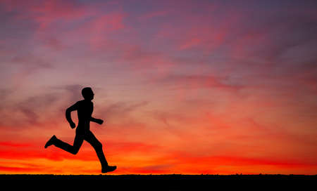 Silhouette of running man against the colorful sky. Silhouette of running man on sunset fiery sky background の写真素材