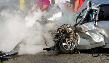 Man extinguishes the car with a fire extinguisher. Damaged vehicle closeup after car crash.の写真素材