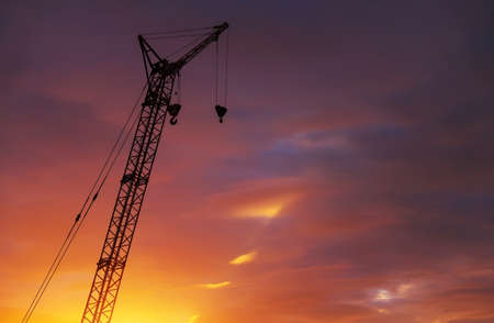Silhouette of high crane with two hooks on fiery sunset sky backgroundの写真素材