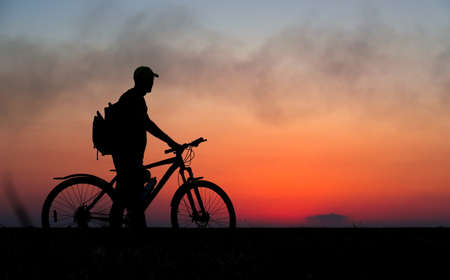 Silhouette of cyclist on the background of red sunset. Biker with bicycle on the field during sunriseの写真素材